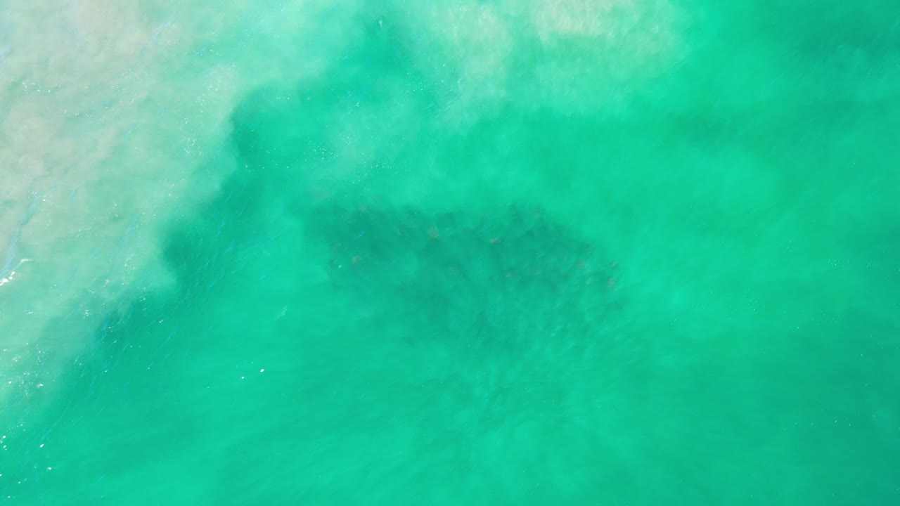 Turquoise ocean water with faint dark fish shapes below the surface