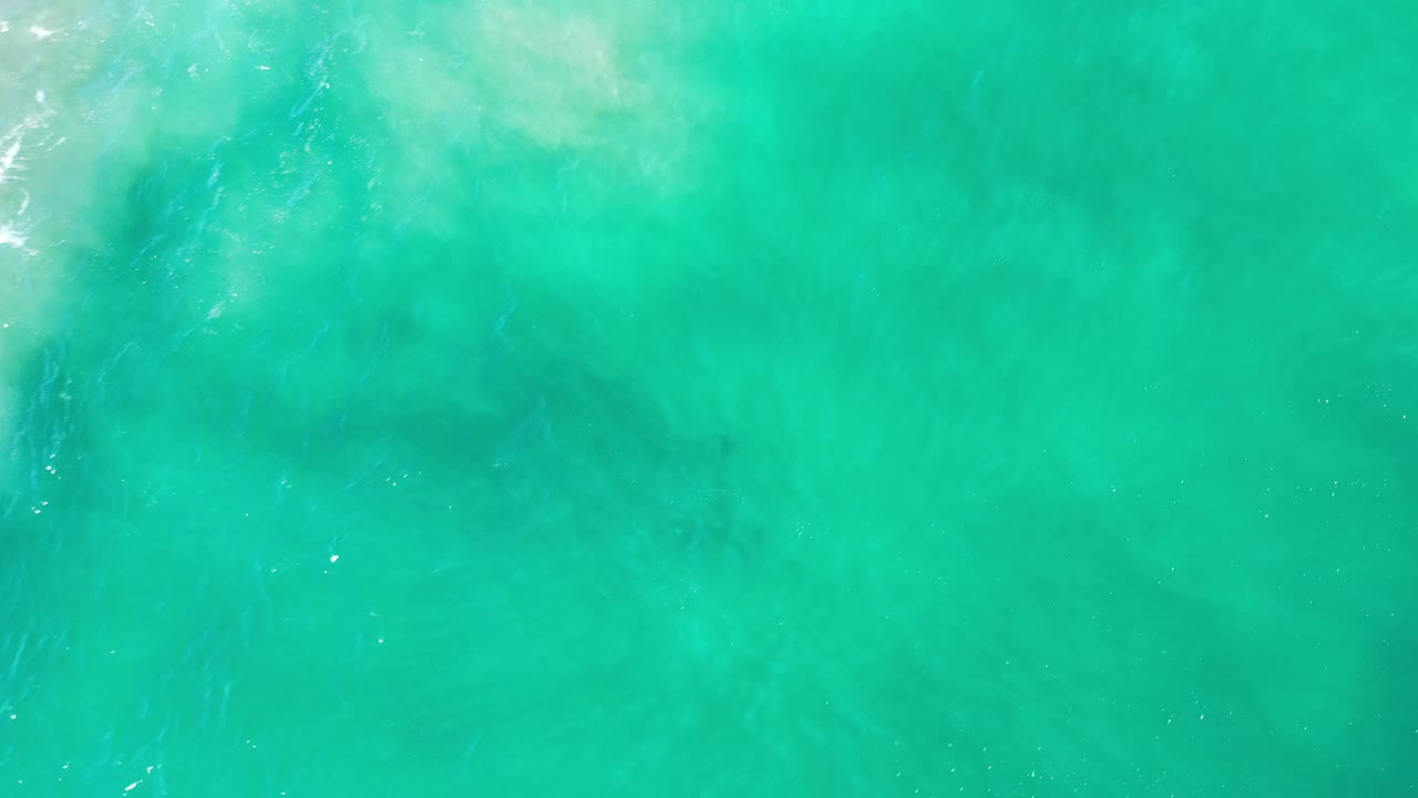 Turquoise ocean surface in Los Cabos, Mexico, seen from above with muted darker patches under the water and no visible people.