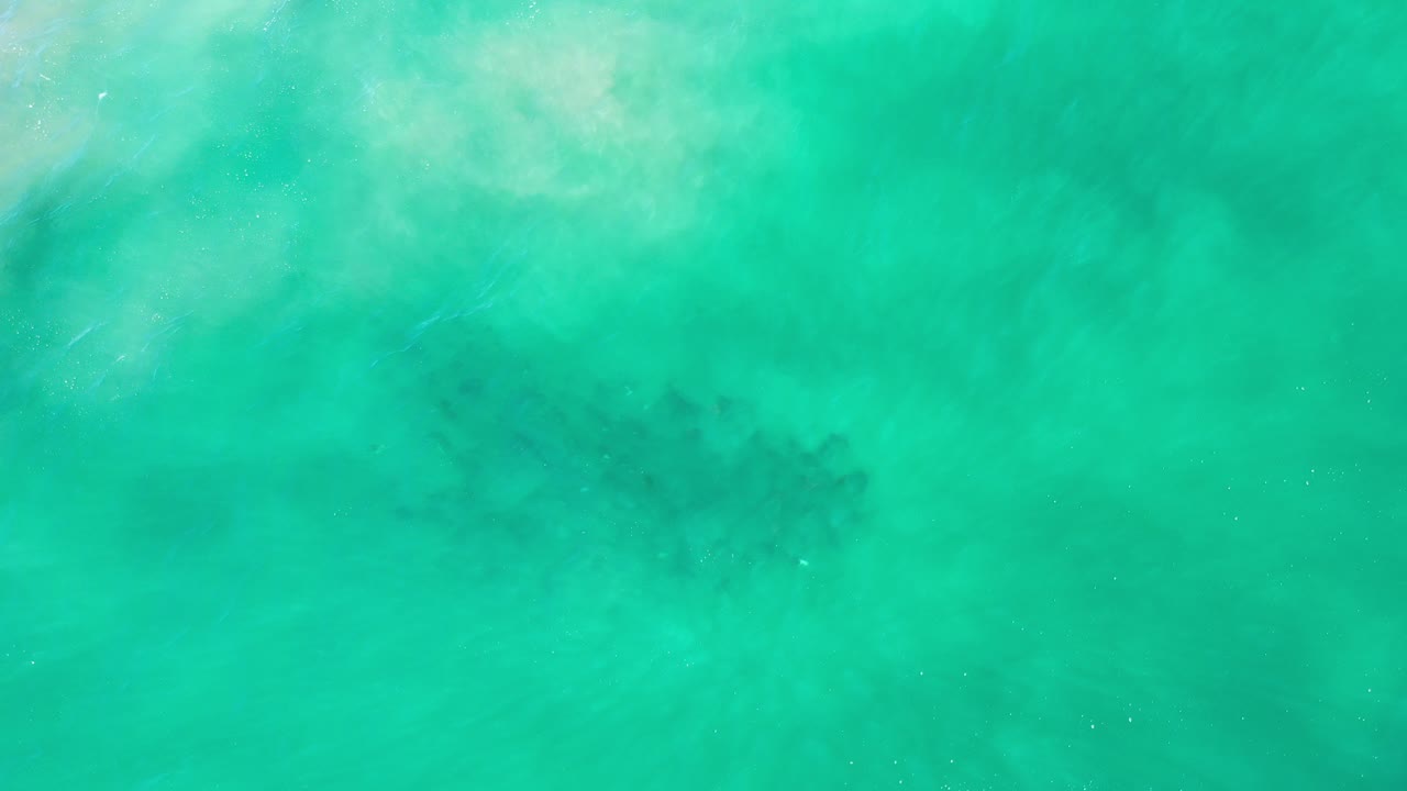 Overhead view of turquoise green sea in Los Cabos with a dark school of fish faintly visible under cloudy surface texture and no visible people.