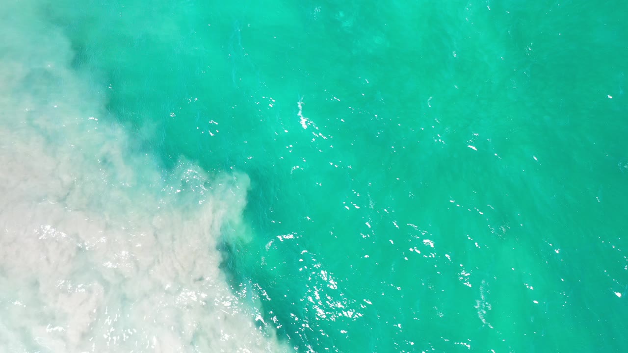 Top-down view of turquoise water in Los Cabos, Mexico, with white seafoam pushing in from the left and no visible people.