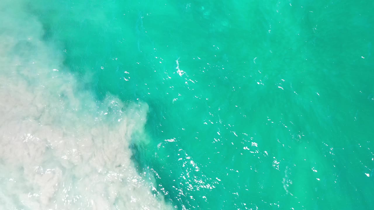 Aqua water in Los Cabos, Mexico, fills the frame while cloudy white surf foam sits along the left side and no visible people appear.