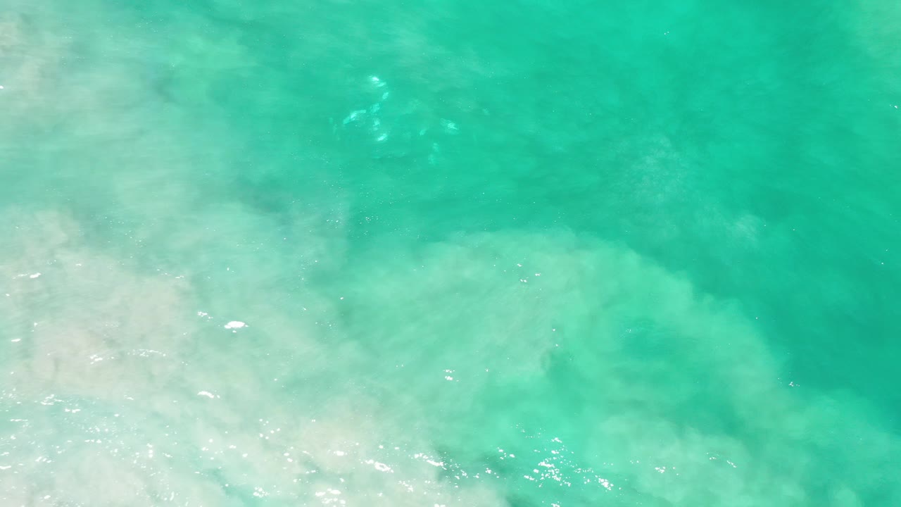 Overhead view of turquoise green seawater in Los Cabos, Mexico, with a pale cloudy foam area across the lower left and no visible people.