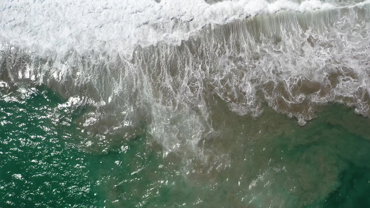 Breaking ocean wave with foamy whitewater over clear green water