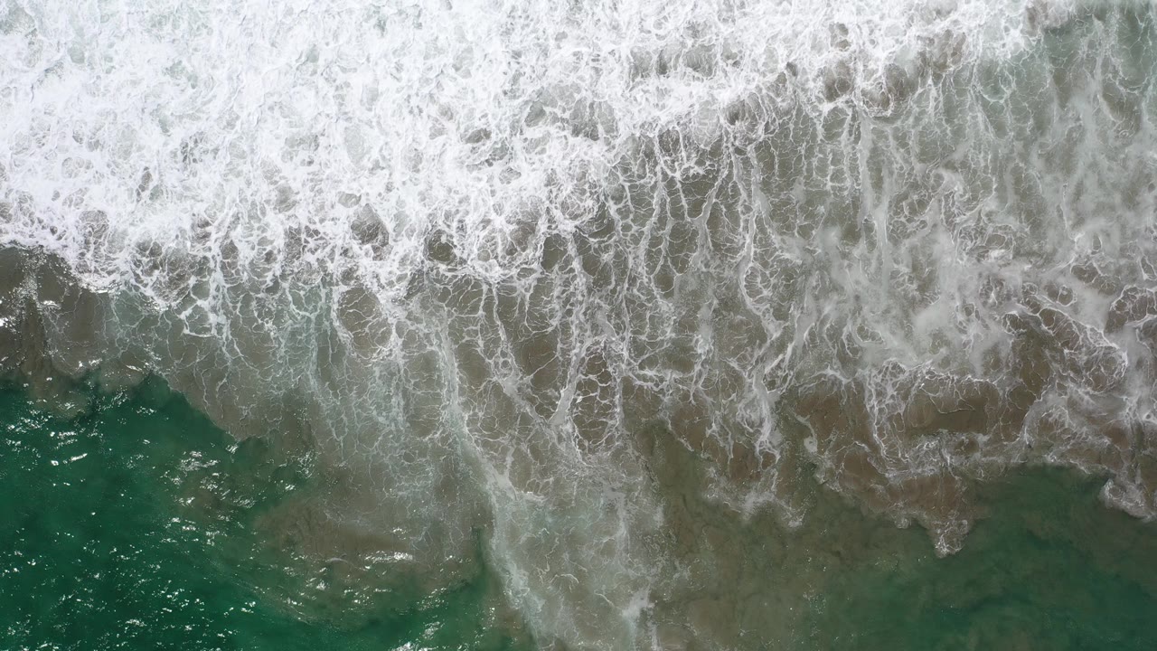 Overhead teal surf and white foam at a sandy shoreline.