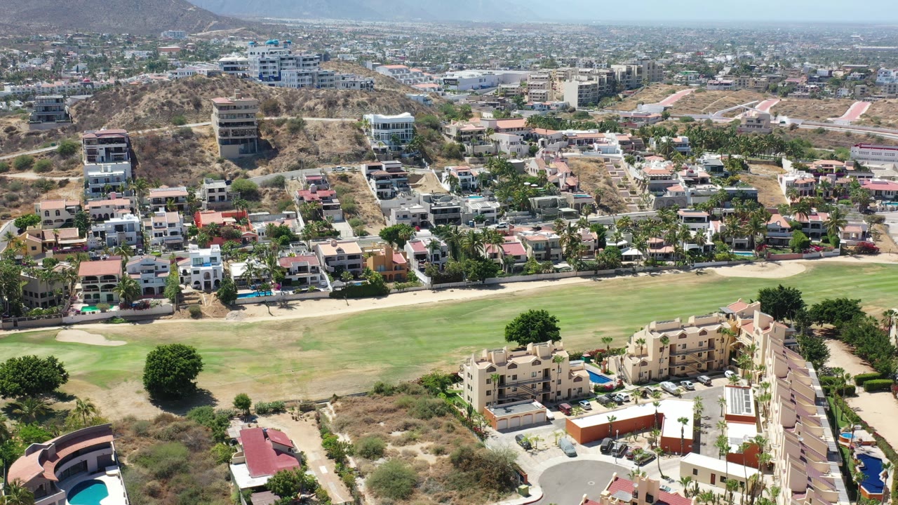 Aerial view of houses beside green grass and dry hills.