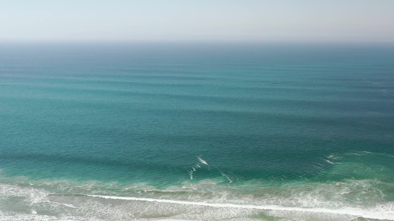 Wide hazy sea view with rolling waves and foam at the shore.