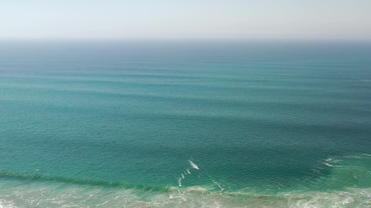 Open ocean with a small diagonal white surf streak near shore.