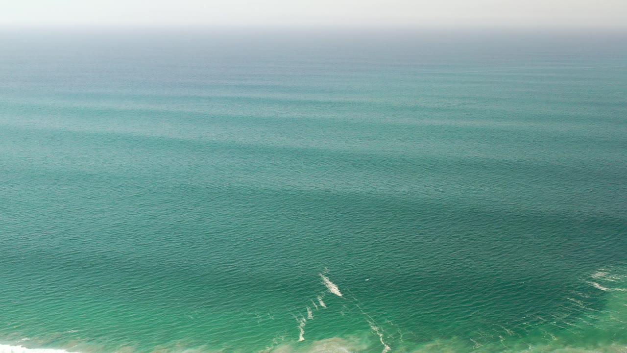 Opening aerial frame over green sea in Los Cabos, Mexico, with a pale horizon band near the top and no visible people.