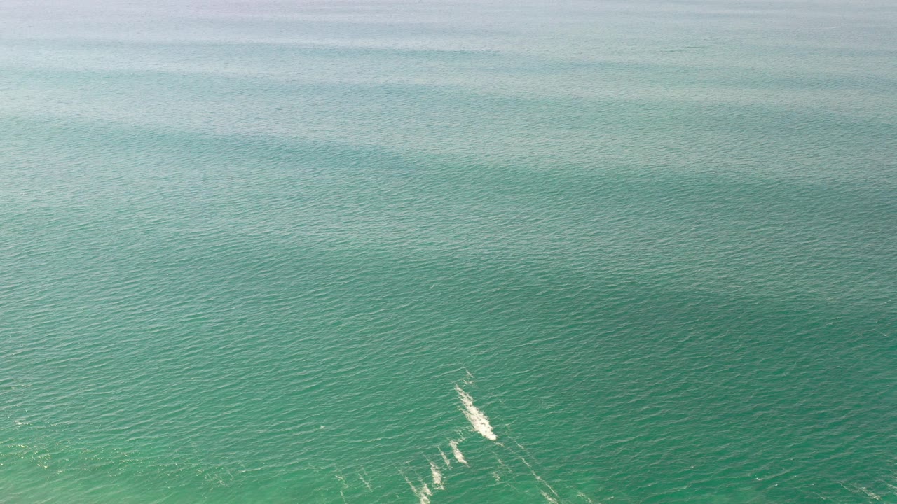 Green ocean surface with small white wave breaks near the lower edge.