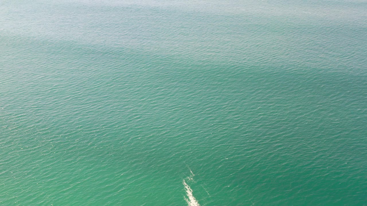 Overhead view of green sea water in Los Cabos, Mexico, with rippled texture, a faint white wake near the lower edge, and no visible people.