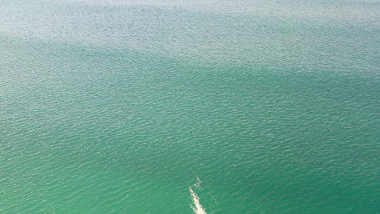 Aerial-looking frame of turquoise-green sea water in Los Cabos, Mexico, with a narrow white streak low in frame and no visible people.