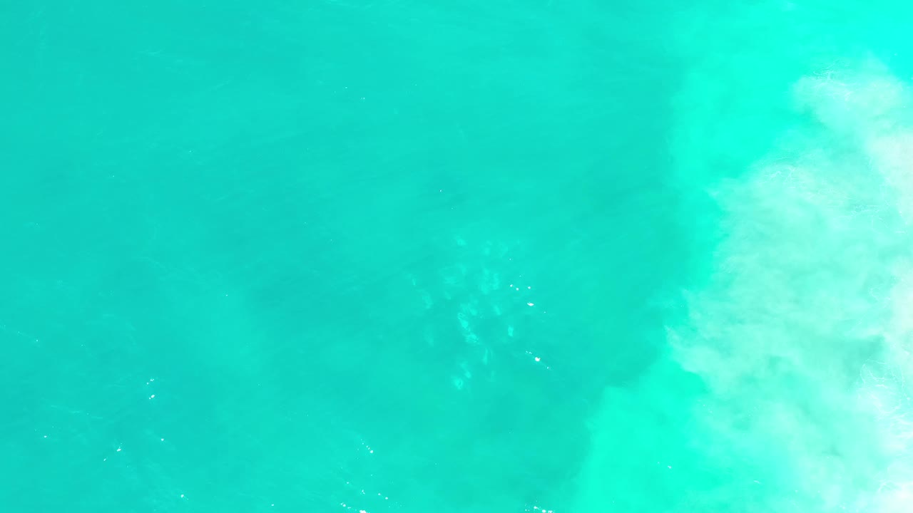 Top-down Los Cabos ocean frame showing green-blue water, small flecks of foam near the center, a brighter surf edge on the right, and no visible people.