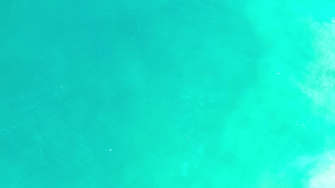 Opening frame of turquoise-green ocean water in Los Cabos, Mexico, with pale cloudy surf or underwater turbulence and no visible people.