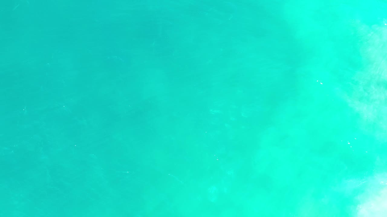 Clear green Los Cabos ocean water fills the frame, with a soft white haze concentrated near the lower edge and no visible people.