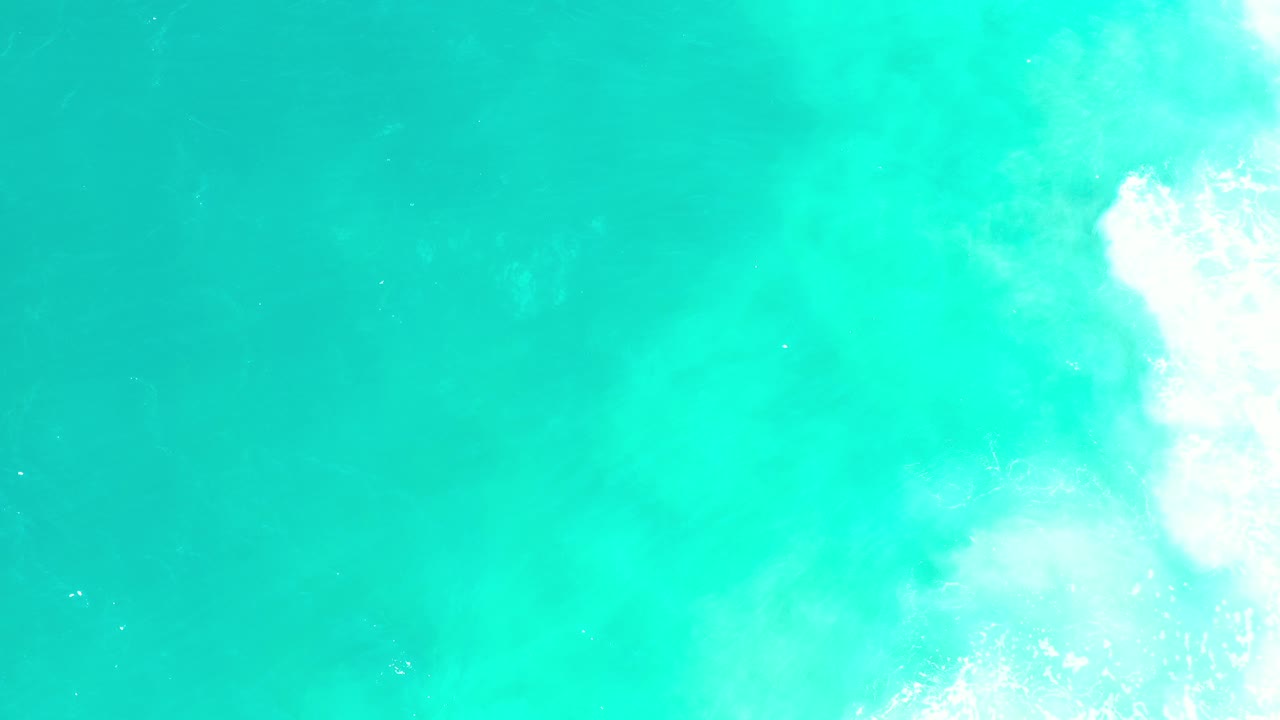 Overhead view of turquoise water in Los Cabos, Mexico, with white surf foam touching the right side and no visible people.
