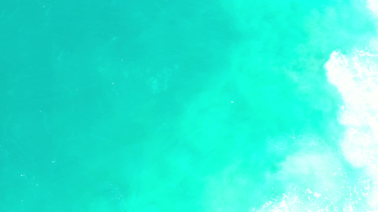 Overhead Los Cabos water frame with blue-green color, faint darker areas below the surface, and surf foam pressed against the right border, with no visible people.