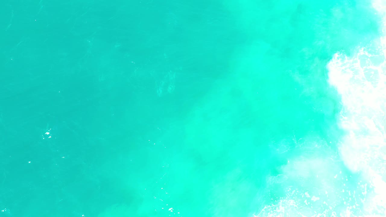 Clear turquoise water with foamy white wave texture at the upper right.