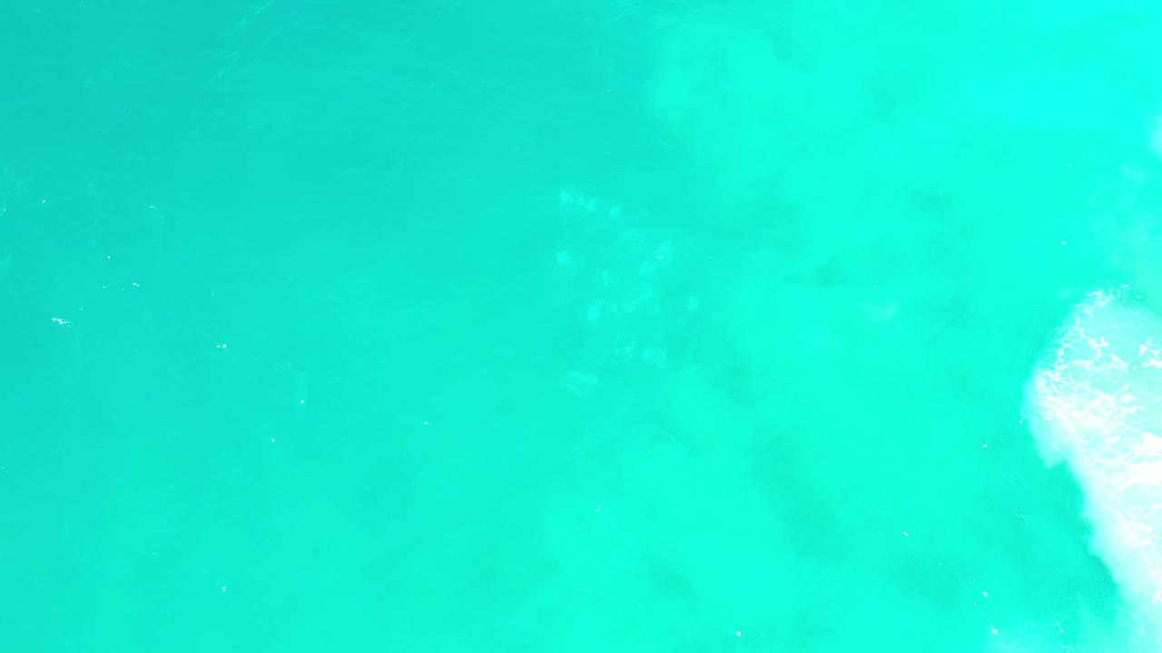 Overhead Los Cabos water frame filled with cyan and turquoise tones, faint pale patches below the surface, and no visible people.