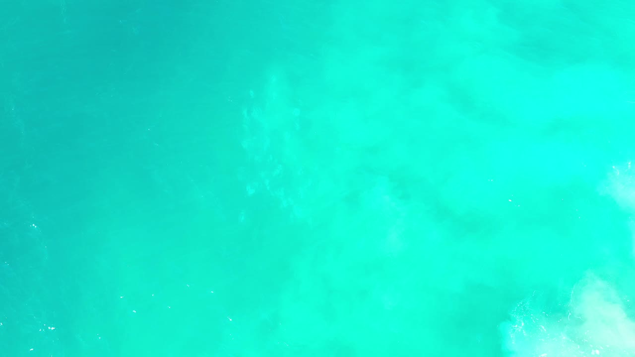 Bright aqua ocean surface with a white foamy patch near the bottom right corner.