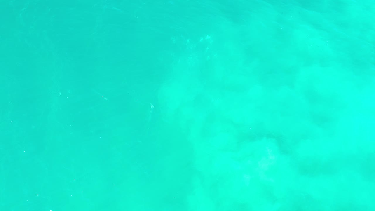 Overhead view of turquoise-green ocean water in Los Cabos, Mexico, with faint pale underwater patches and no visible people.