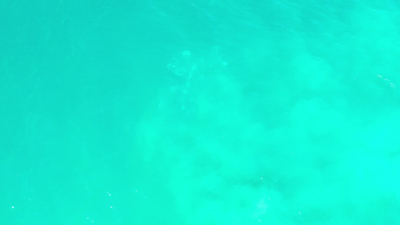 Overhead view of green-blue water over pale sand in Los Cabos, Mexico, with soft underwater texture and no visible people.