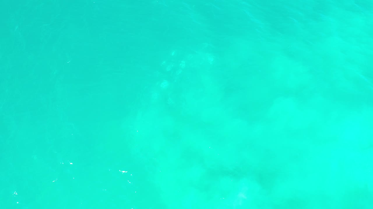 Bright turquoise ocean surface with cloudy sand forms underneath.