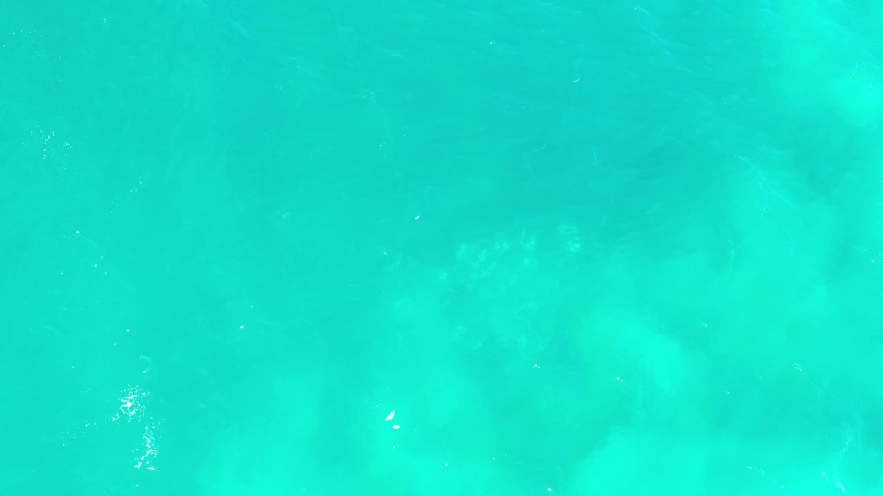Overhead Los Cabos water frame with a smooth turquoise surface, faint ripples, small sunlight specks, and no visible people.