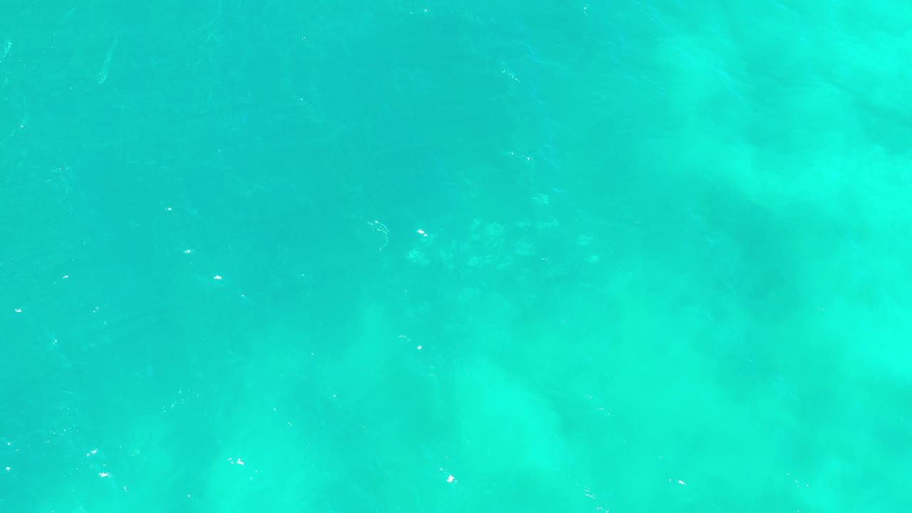 Overhead turquoise water in Los Cabos, Mexico, with soft underwater color patches, tiny surface highlights, and no visible people.