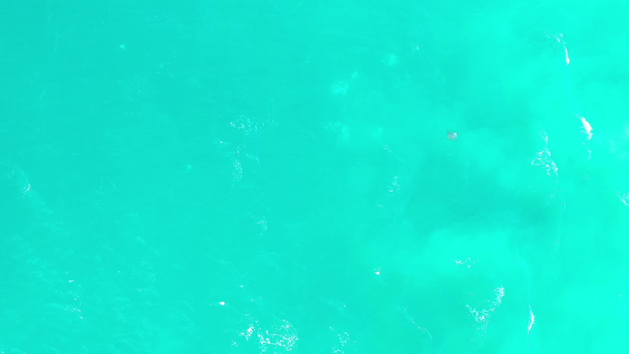 Overhead view of bright turquoise sea water in Los Cabos, Mexico, with pale underwater sand patches and no visible people.