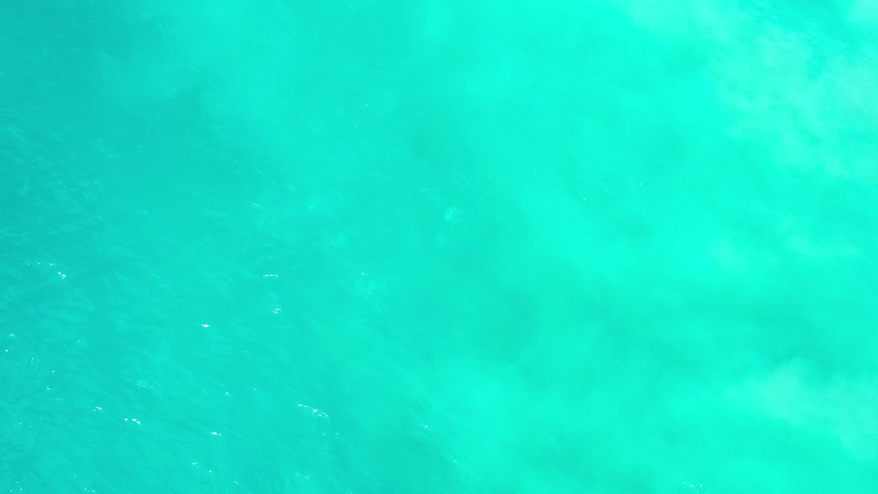 Direct overhead view of turquoise water in Los Cabos, Mexico, with soft pale wave bands and no visible people.