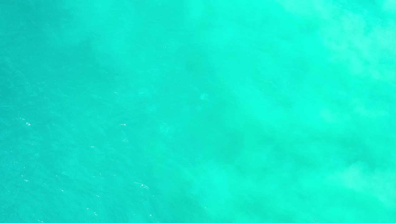 Overhead Los Cabos ocean frame with bright aqua water, scattered white shimmer, and no visible people or shoreline.