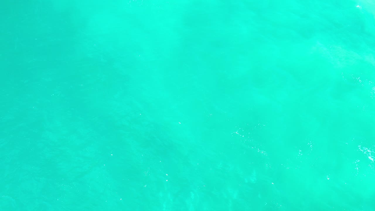 Top-down view of bright turquoise water in Los Cabos, Mexico, with faint underwater texture and no visible people.