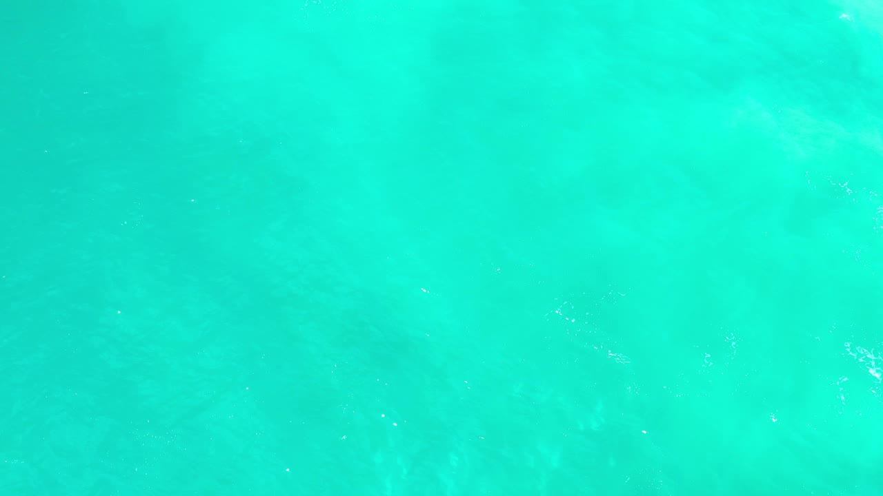 Overhead Los Cabos water frame with blue-green color, soft subsurface patches, tiny pale specks, and no visible people.