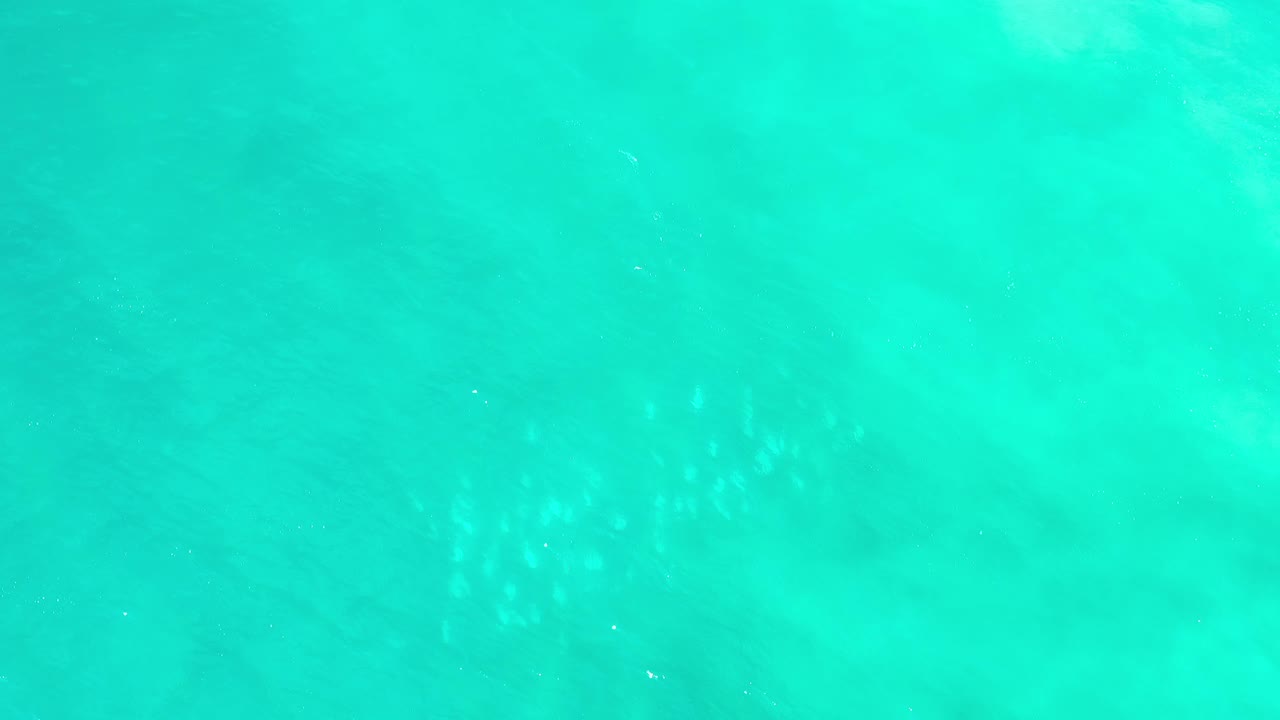 Aerial frame of blue-green water in Los Cabos, Mexico, with faint white surface ripples crossing the otherwise open water and no visible people.