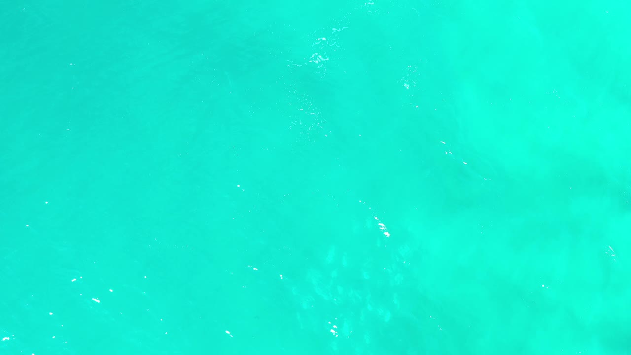 Overhead view of turquoise green water in Los Cabos, Mexico, with faint pale patches under the surface and no visible people.