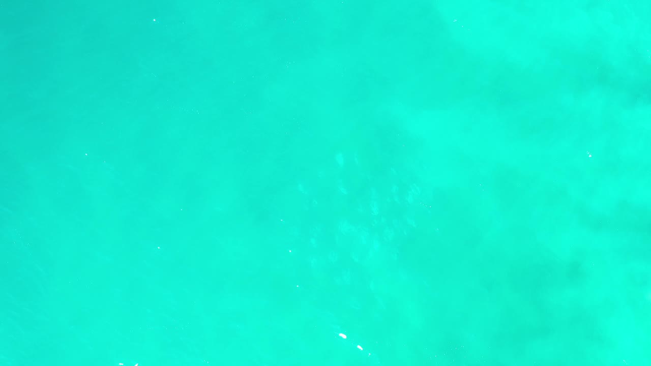 High aerial view of blue-green water in Los Cabos, Mexico, with soft seafloor color variation and no visible people.