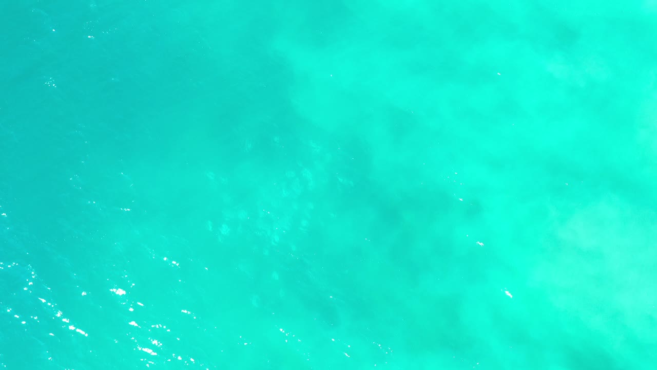 Bright turquoise ocean water in Los Cabos, Mexico fills the frame with faint darker patches below the surface and no visible people.
