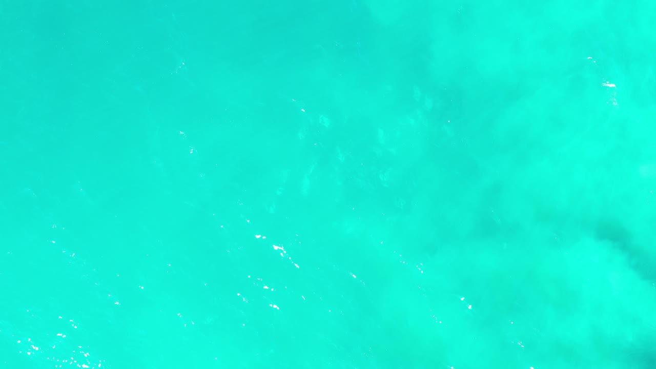 Overhead view of clear turquoise ocean in Los Cabos, Mexico, with soft lighter patches under the surface and no visible people.
