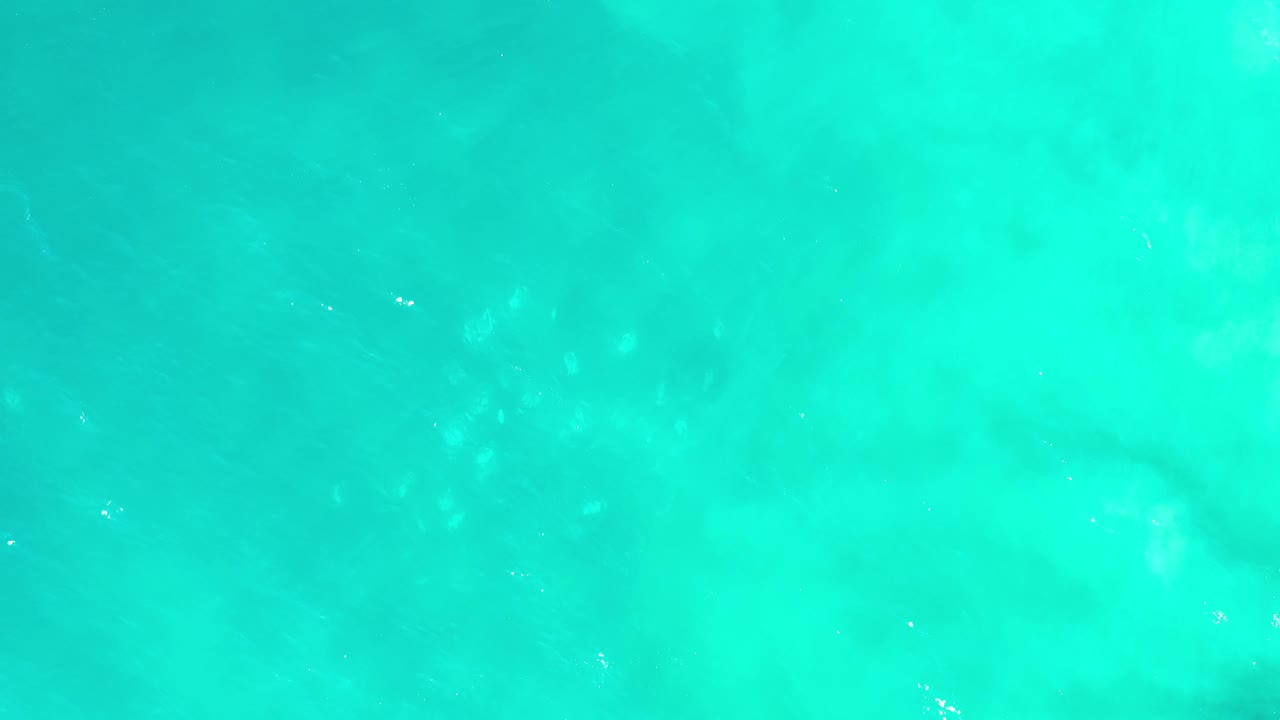Bright green ocean surface in Los Cabos, Mexico shows cloudy darker areas beneath the water and tiny white ripple highlights, with no visible people.