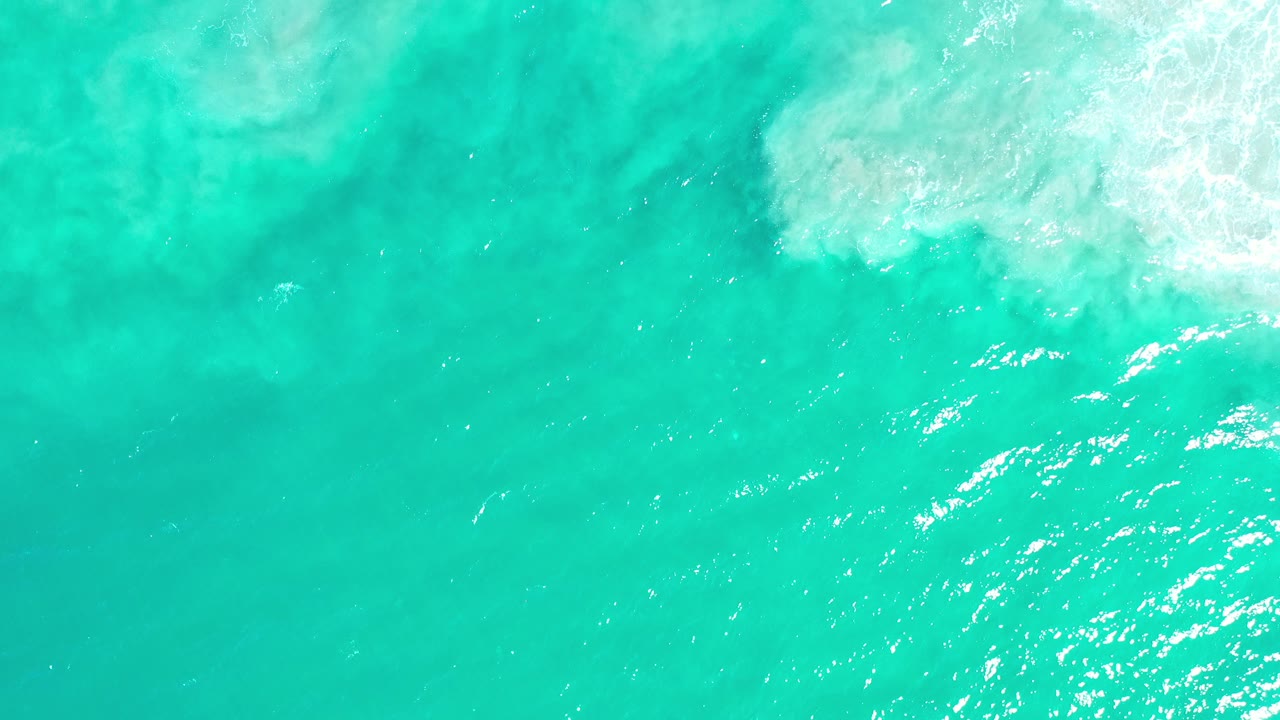 Turquoise ocean water with white foam at the upper right