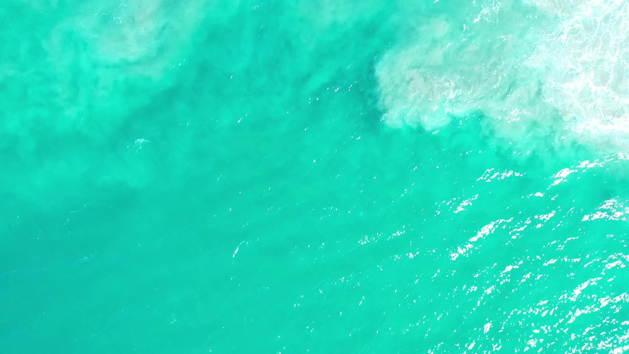 Overhead Los Cabos water frame with pale foam near the top right, darker green patches beneath the surface, and no visible people.