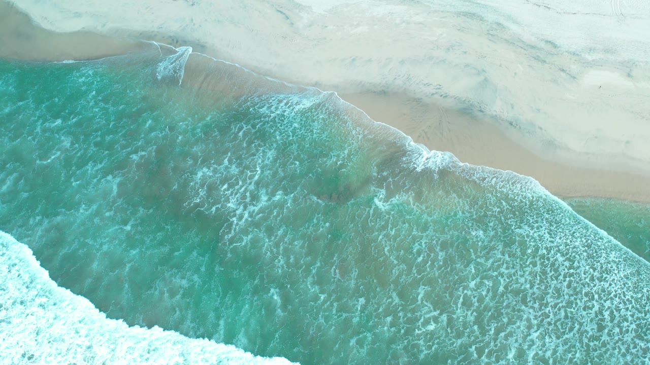 Turquoise water and white foam spread diagonally across the Los Cabos shoreline, with no visible people.