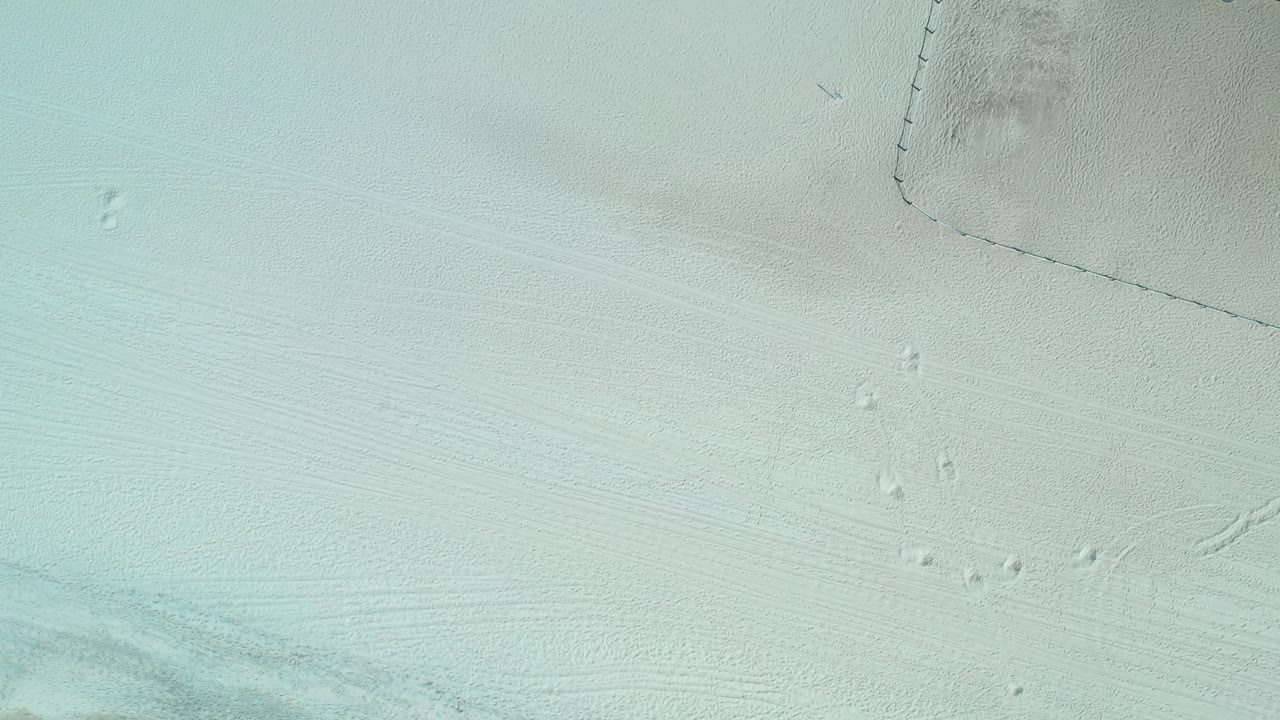 Aerial Los Cabos beach view with pale sand, small footprint marks, a fence boundary near the top, and no visible people.