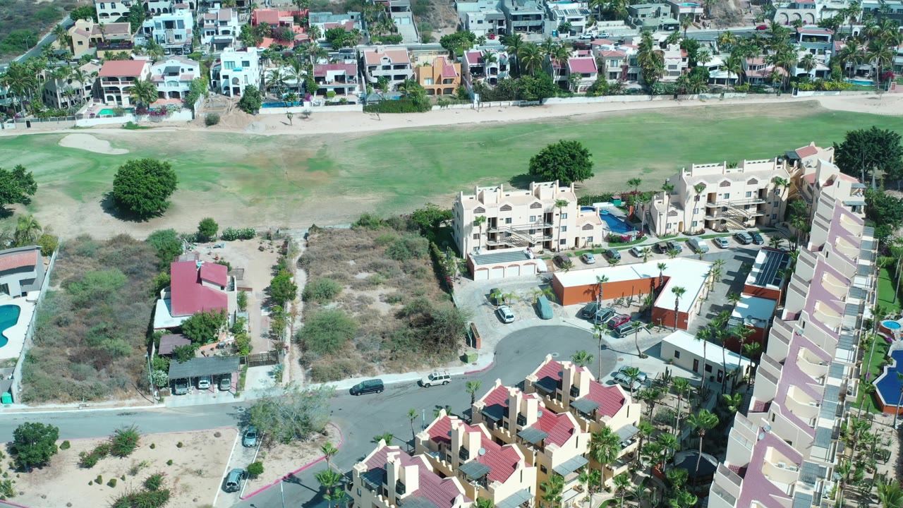 Aerial neighborhood view with field, homes, and parked cars.