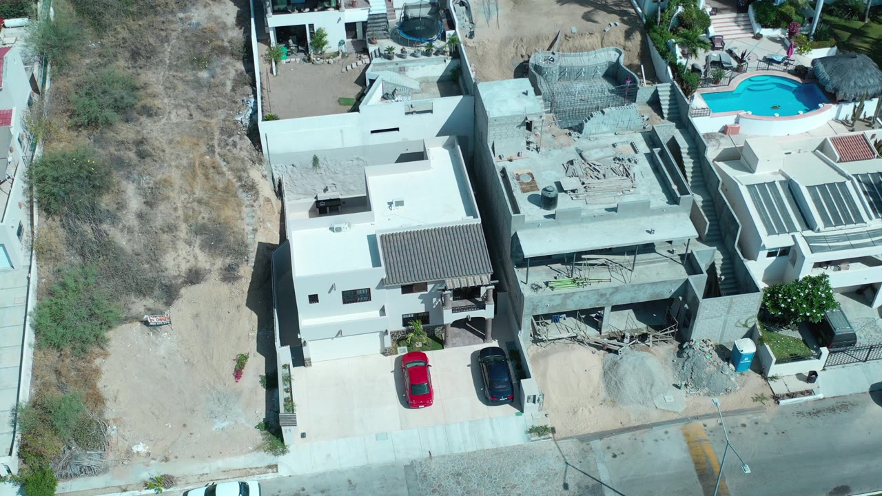 Overhead view of homes, a driveway, and two parked cars beside a dry lot.