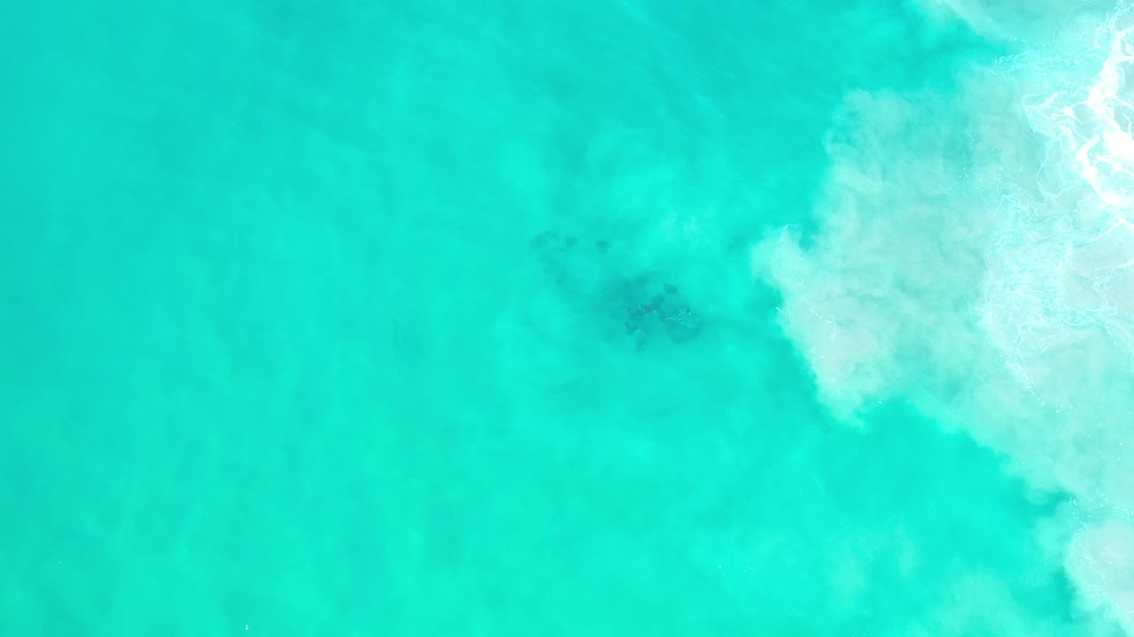 Pale turquoise sea with faint fish shadows and white foam along the right side.