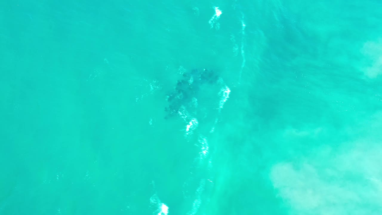 Turquoise ocean surface with white foam streaks and a dark reef-like patch.