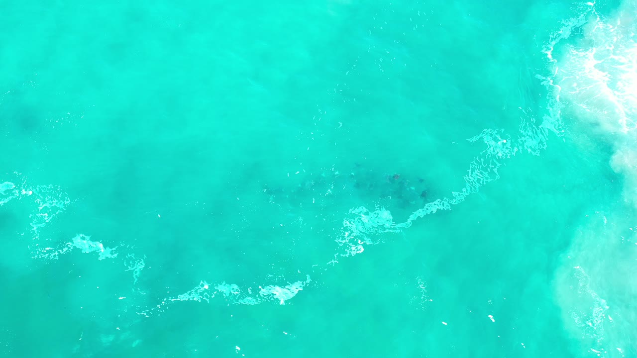Top-down view of turquoise-green sea in Los Cabos, Mexico, with white surf foam entering from the right and no visible people.