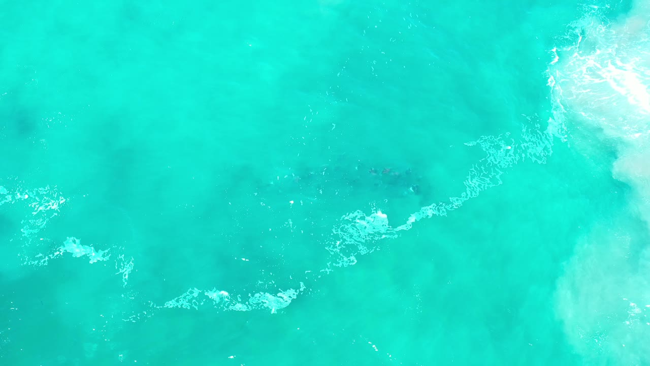 Aerial view over turquoise sea in Los Cabos, Mexico, with a bright surf wash on the right and no visible people.