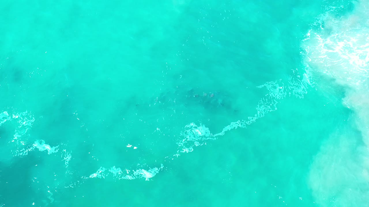 Top-down Los Cabos ocean view with pale foam traces, soft green water, darker underwater patches, and no visible people.